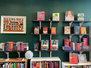A photo of a bookshop wall, with art on te left and 7 floating shelves filled with books.